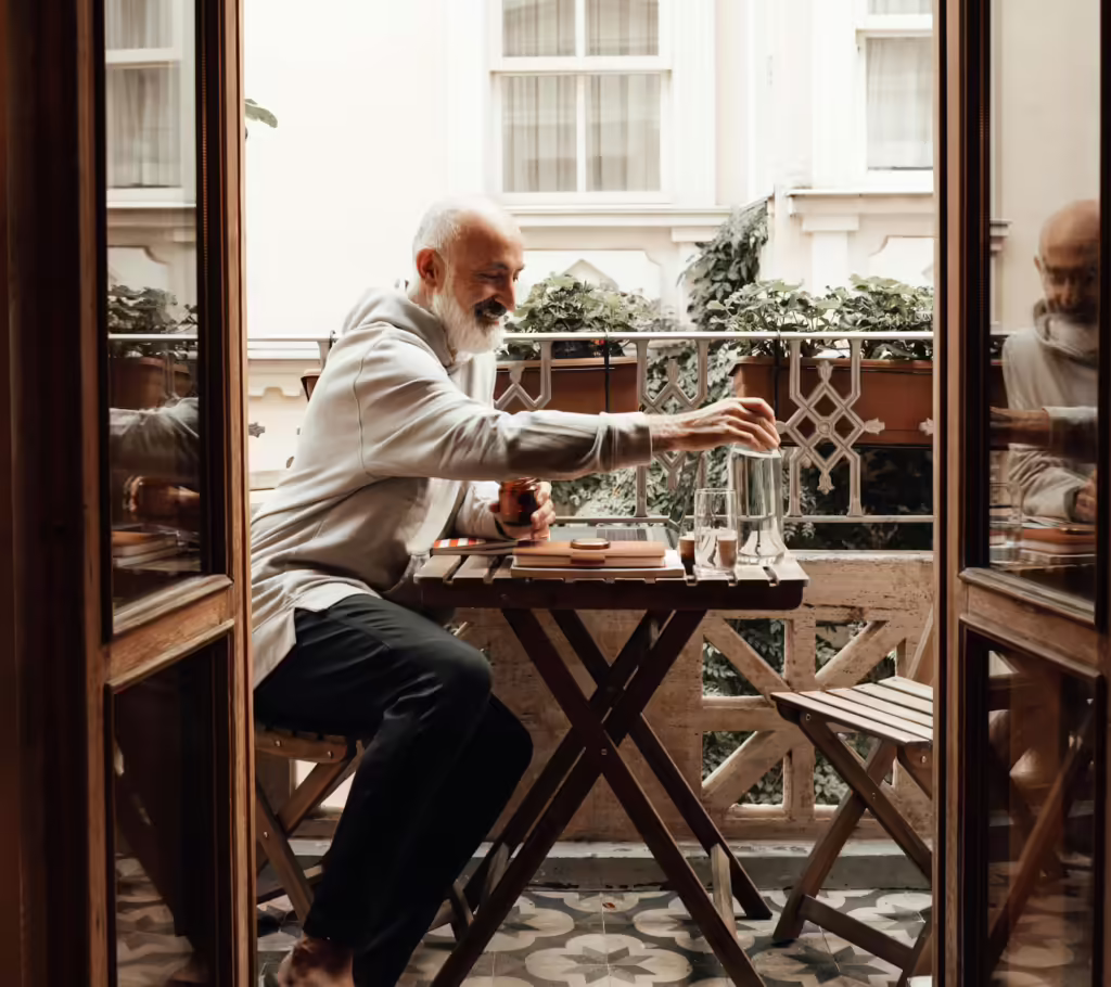 A man with a beard sitting at an outdoor table, pouring water into a glass.