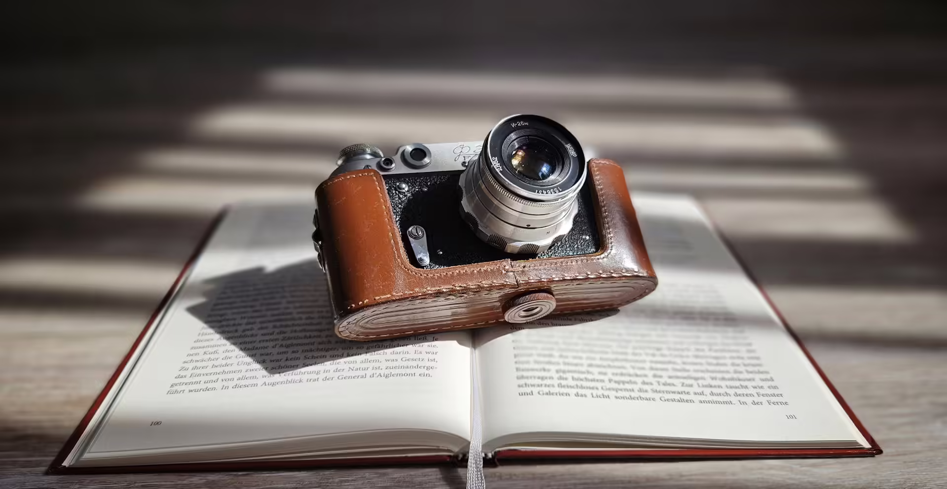 A vintage camera resting on an open book, with soft sunlight filtering through the background.