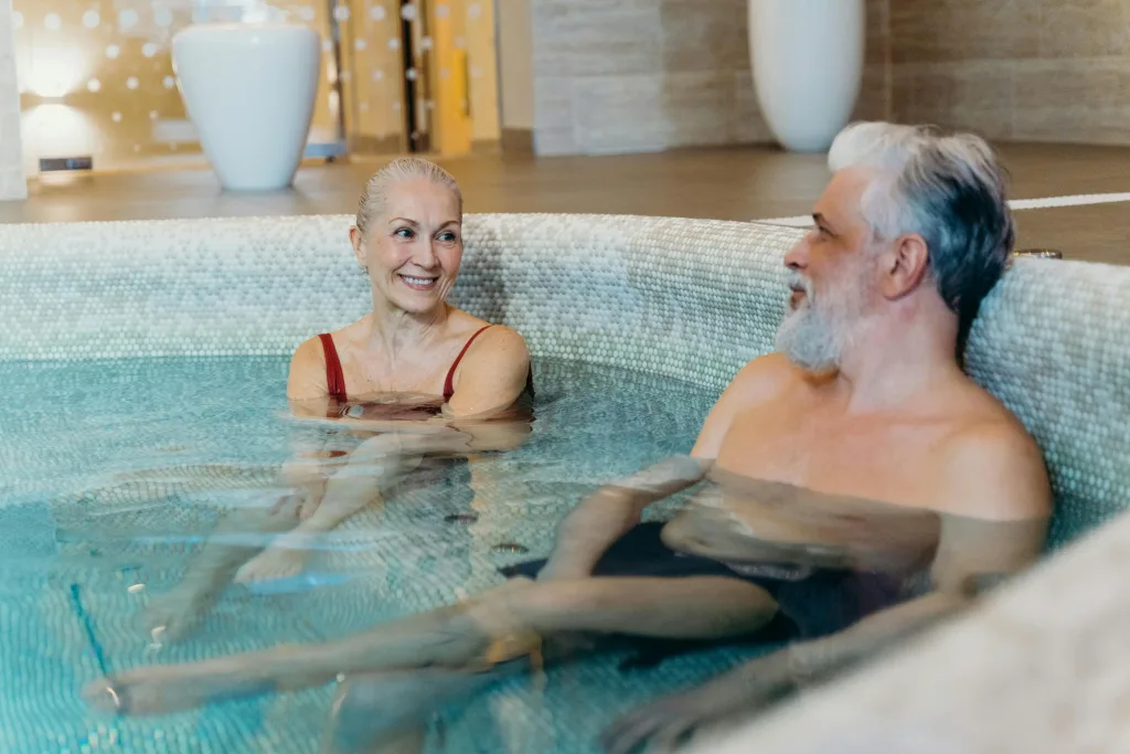 A senior couple enjoying a relaxing moment in a warm indoor spa pool, smiling and engaging in conversation.