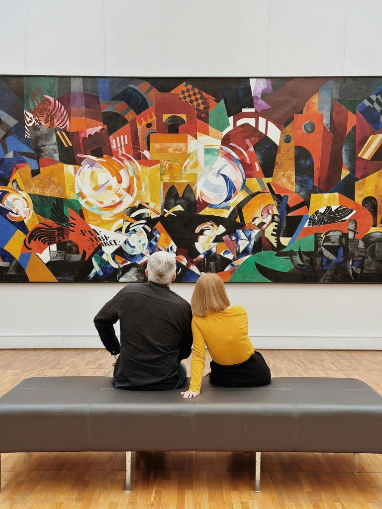 A couple sitting on a bench in an art gallery, admiring a vibrant abstract painting.